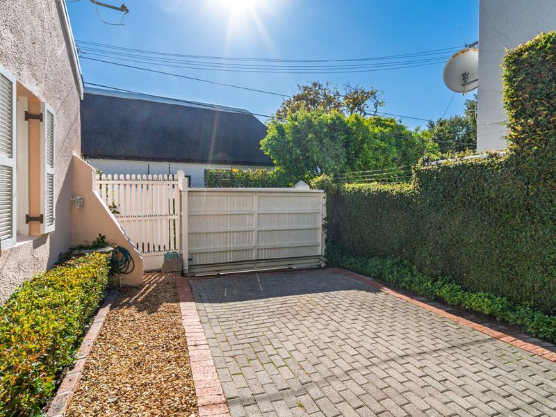 A private paved driveway entrance featuring a sliding gate, picket fencing, and established perimeter hedging.