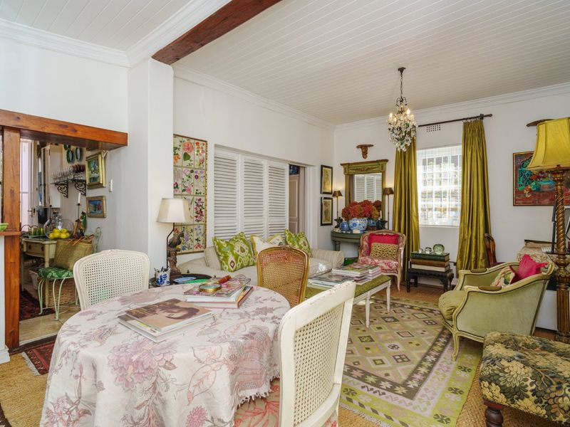 An open-plan living and dining area featuring a timber-beamed tongue and groove ceiling, plantation shutters, and a classic crystal chandelier.