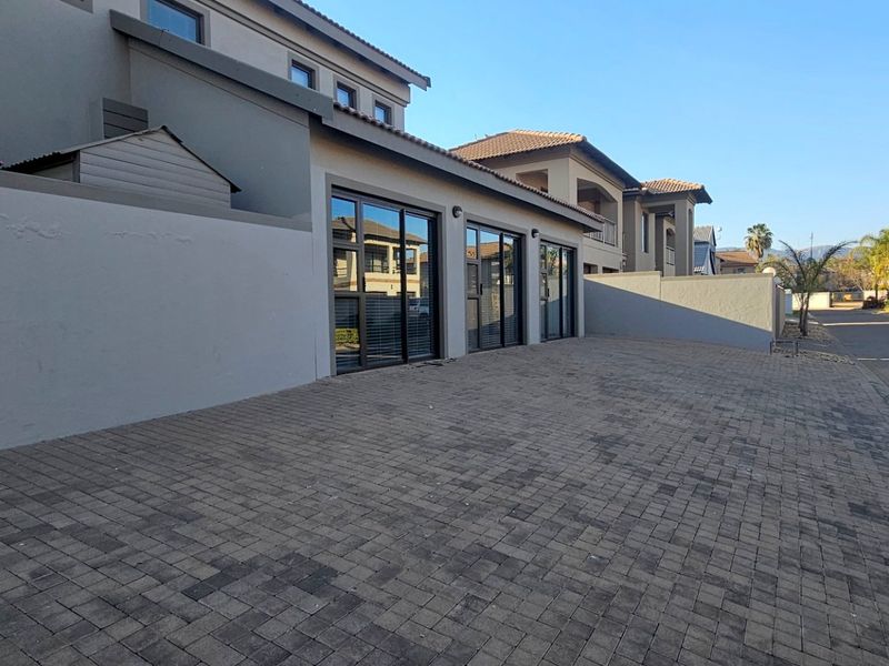 Front exterior view of the property featuring a paved driveway, boundary wall, and modern aluminium framed sliding doors leading into the home.