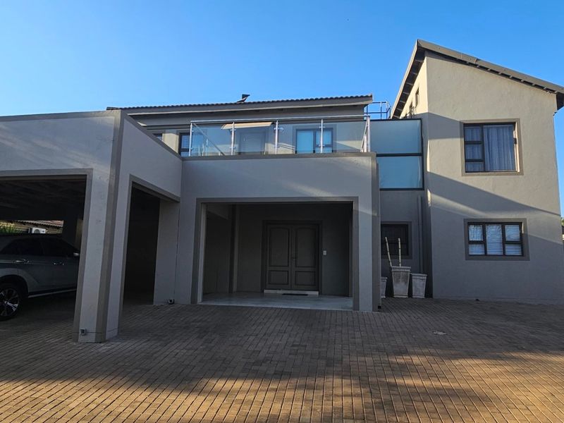 Modern double-storey residential property featuring a paved driveway, integrated double garage, and an upper-level balcony with glass balustrades.
