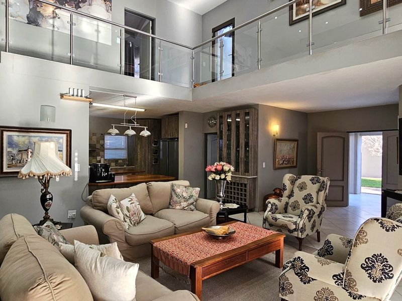 Spacious open-plan living area featuring a double-volume ceiling, glass balustrade mezzanine, and integrated wine storage, creating a bright and airy atmosphere.