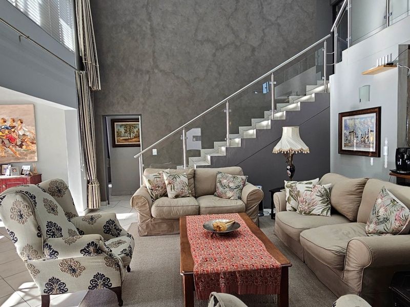 Spacious open-plan living area featuring a double-volume ceiling, modern staircase with glass balustrade, and integrated kitchen space with contemporary finishes.