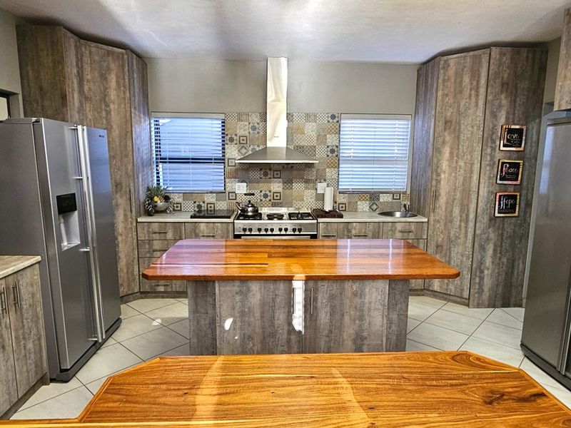 Modern kitchen featuring wood-look cabinetry, a central island with a timber countertop, stainless steel appliances, and a decorative tiled splashback.