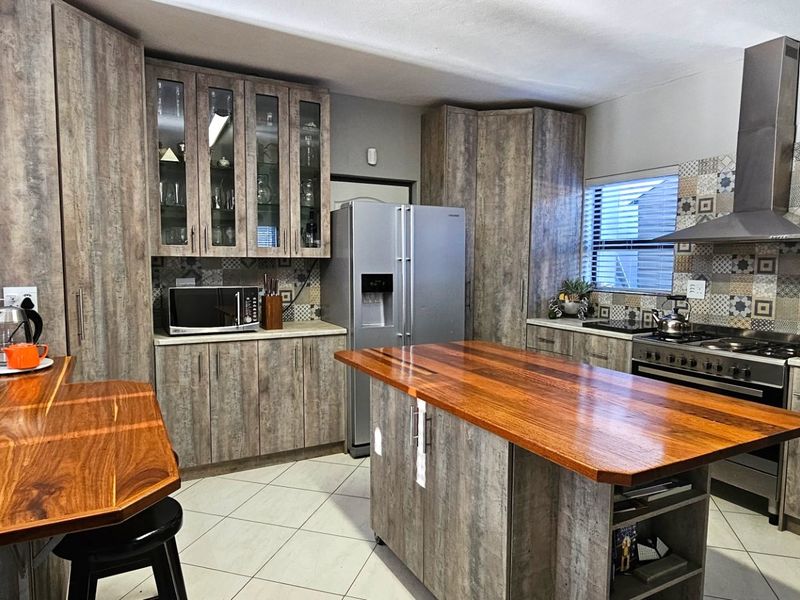 Modern kitchen featuring wood-look cabinetry, timber countertops, a central island, and a stainless steel extractor fan with a decorative tiled backsplash.