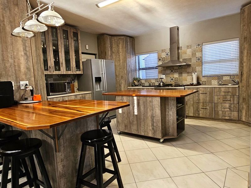 A well-appointed kitchen featuring wood-look cabinetry, a central island with a wooden countertop, a breakfast bar, and a decorative tiled backsplash.