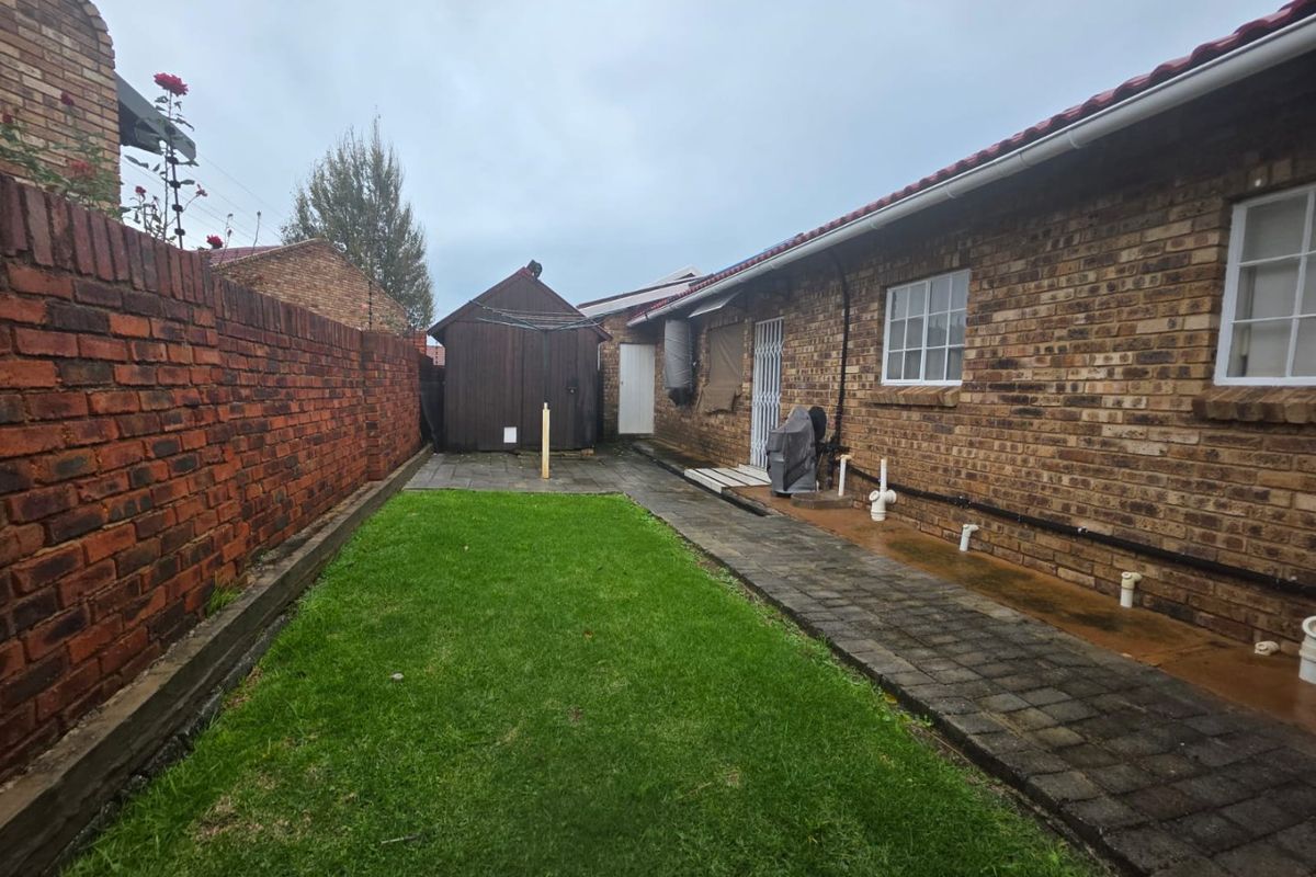 A private rear garden featuring a paved walkway, a small lawn area, and a detached wooden storage shed against a brick boundary wall.