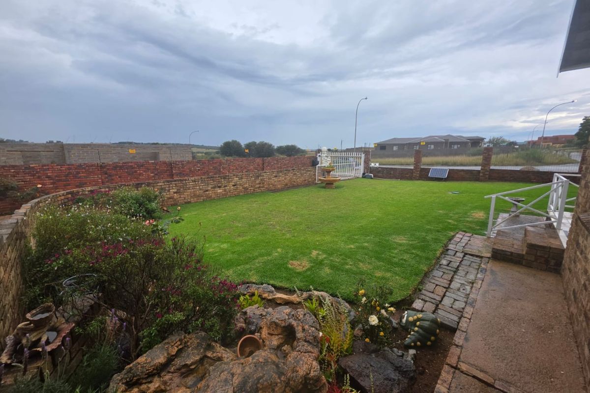 A well-maintained rear garden featuring a manicured lawn, brick boundary walls, a paved walkway, and a decorative rock feature.