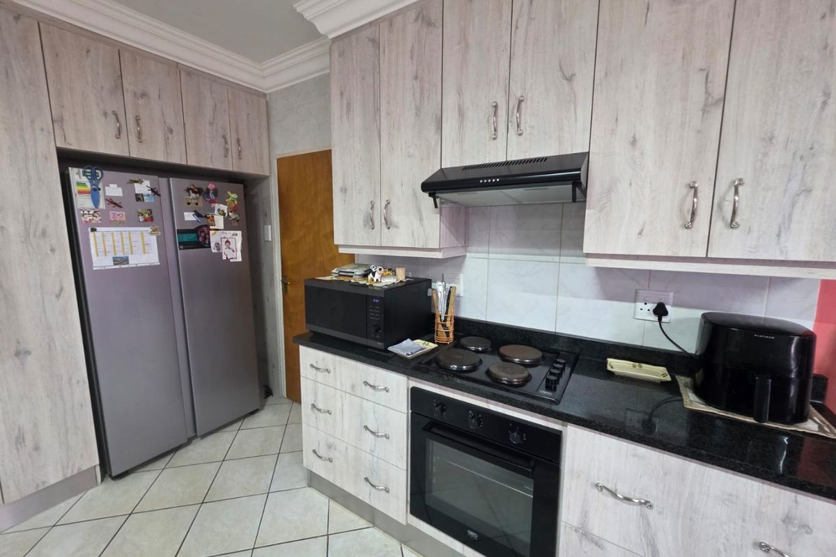 Functional kitchen featuring light wood-grain cabinetry, dark granite countertops, built-in oven, electric hob, and extractor fan with tiled flooring.