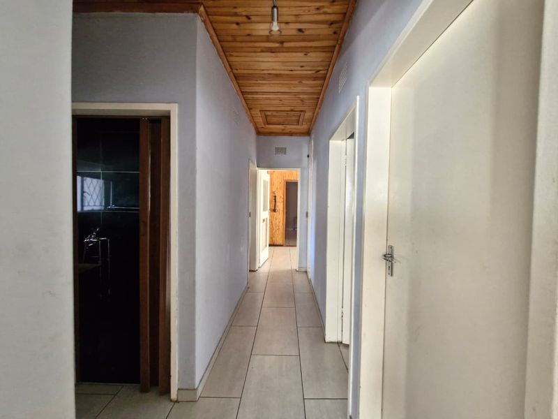 A functional hallway featuring tiled flooring and a timber tongue and groove ceiling, providing access to multiple rooms within the home.