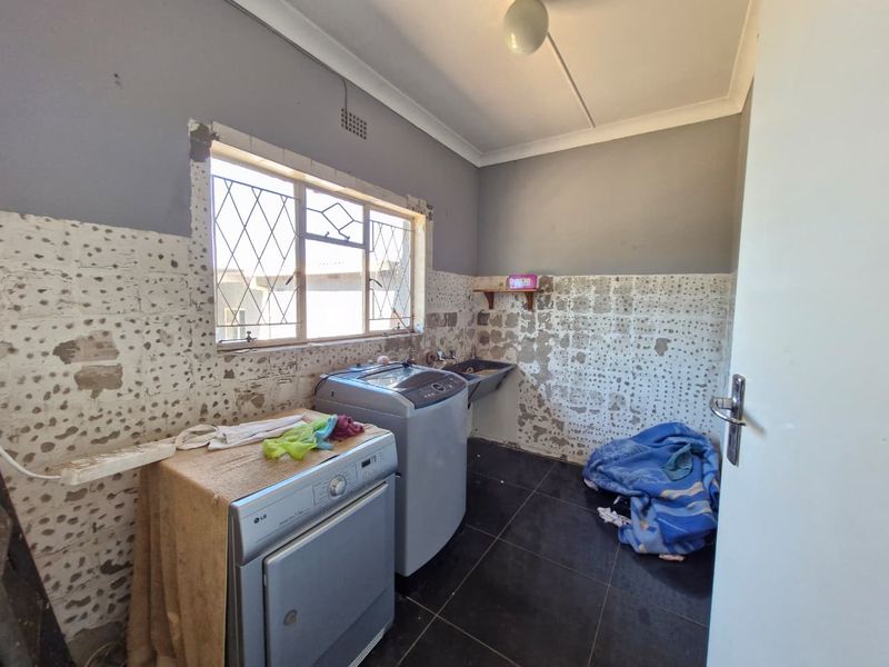 A laundry room featuring dark floor tiles and a utility sink, currently requiring wall repairs and finishing to complete the space.