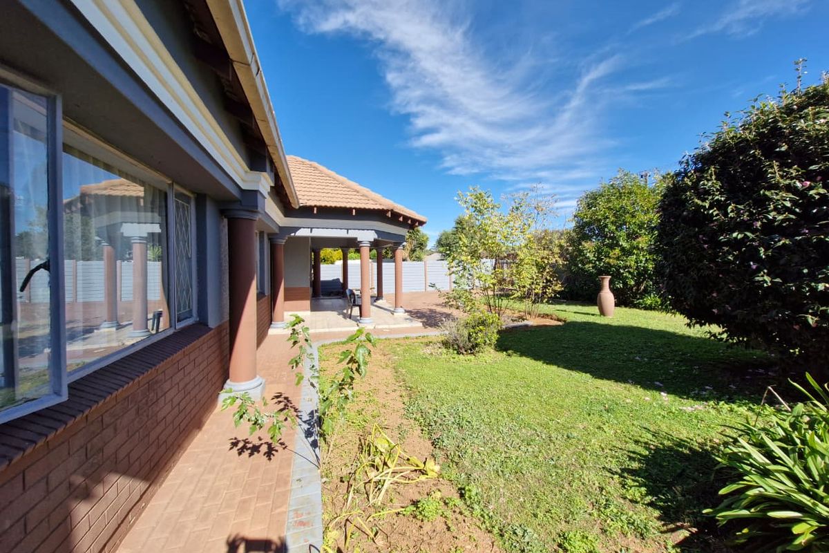 A view of the rear garden featuring a covered patio with concrete columns, brick paving, and a well-maintained lawn area.