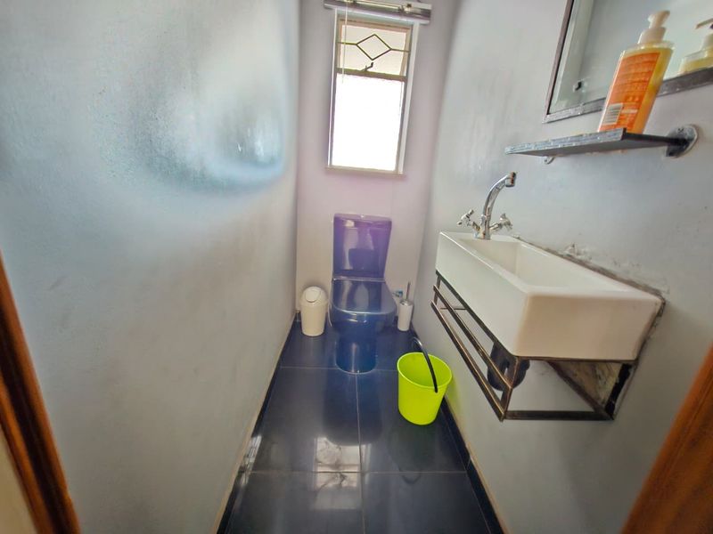 A compact guest bathroom featuring a wall-mounted basin, modern toilet, and dark tiled flooring, providing a functional and minimalist space.