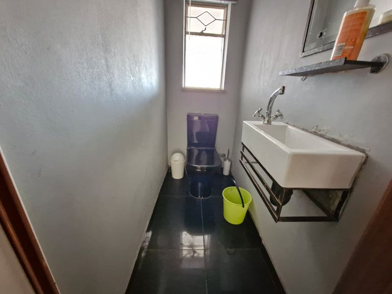 A compact guest bathroom featuring a wall-mounted basin, chrome tapware, and dark floor tiles, requiring minor cosmetic updates to the wall finish.