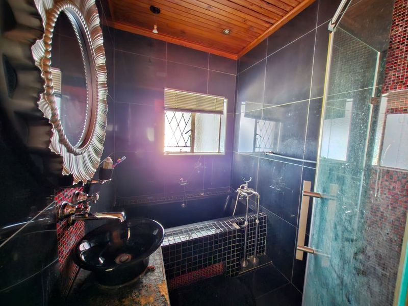 A bathroom featuring dark tiled walls, a built-in bathtub, a glass shower enclosure, and a timber ceiling with a vessel sink vanity.