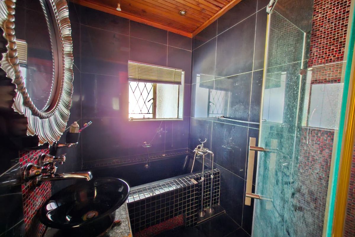 A compact bathroom featuring dark tiled walls, a built-in bathtub, a glass shower enclosure, and a timber ceiling.
