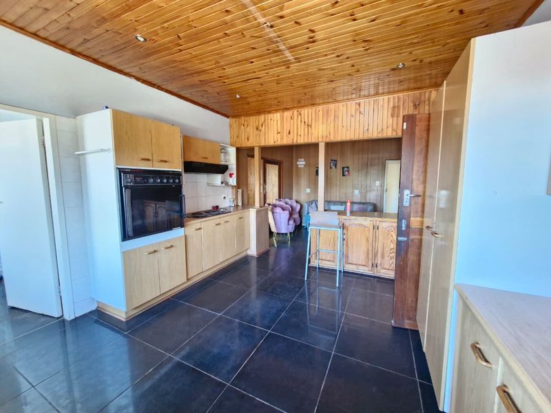 Open-plan kitchen and living area featuring timber ceiling and wall paneling, dark tiled flooring, and built-in cabinetry with integrated oven and hob.