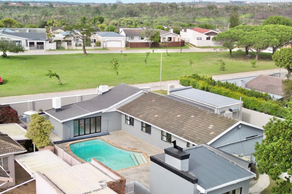 Aerial view of a residential property featuring a swimming pool, paved patio area, and multiple roof structures in a suburban setting.