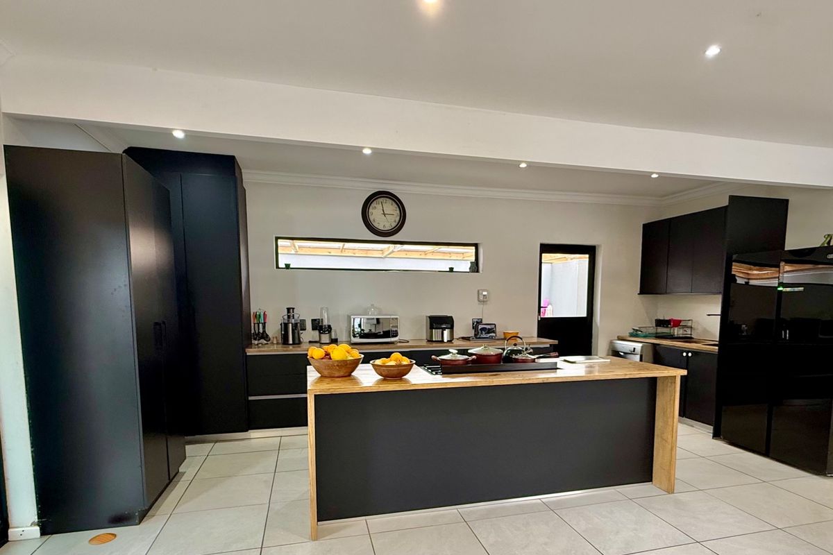 Modern kitchen featuring dark cabinetry, a central island with a wooden countertop, tiled flooring, and recessed lighting.