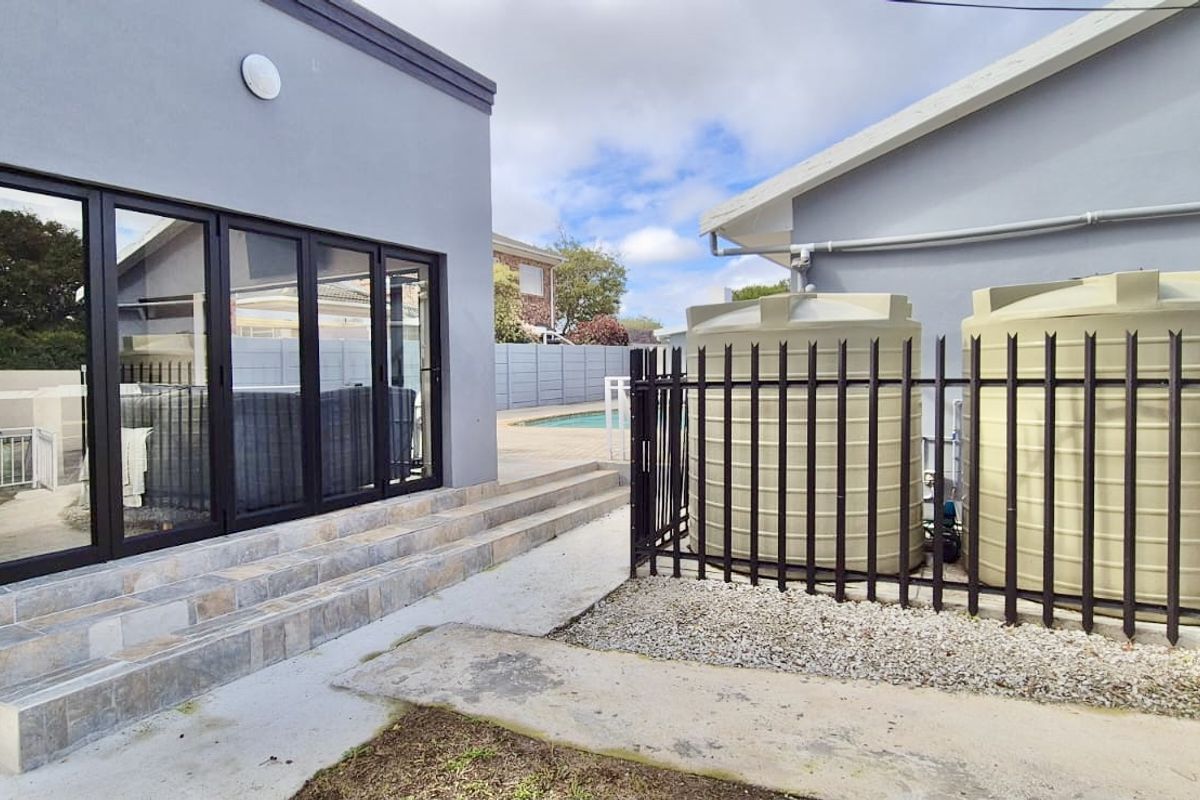 Rear exterior view featuring tiled steps leading to bi-fold doors, with installed water storage tanks and security fencing in the side yard area.