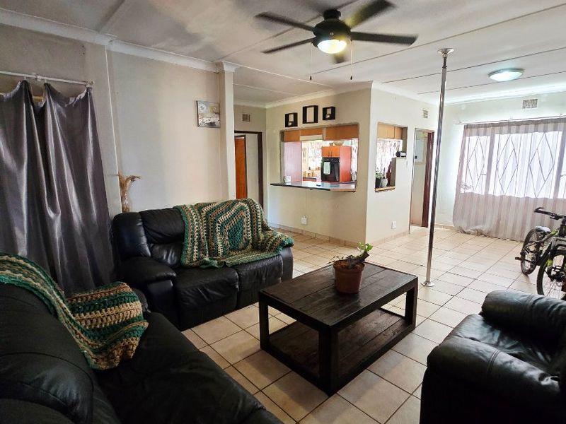 Open-plan living area featuring tiled flooring, a ceiling fan, and a kitchen pass-through window, offering a functional layout with potential for modernization.