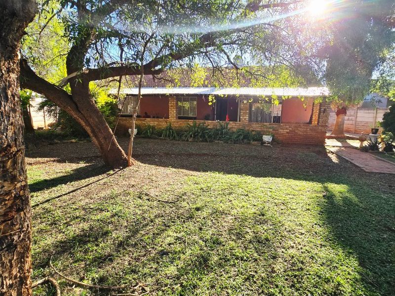 A view of the rear garden featuring a brick-faced house with a covered patio and mature trees.