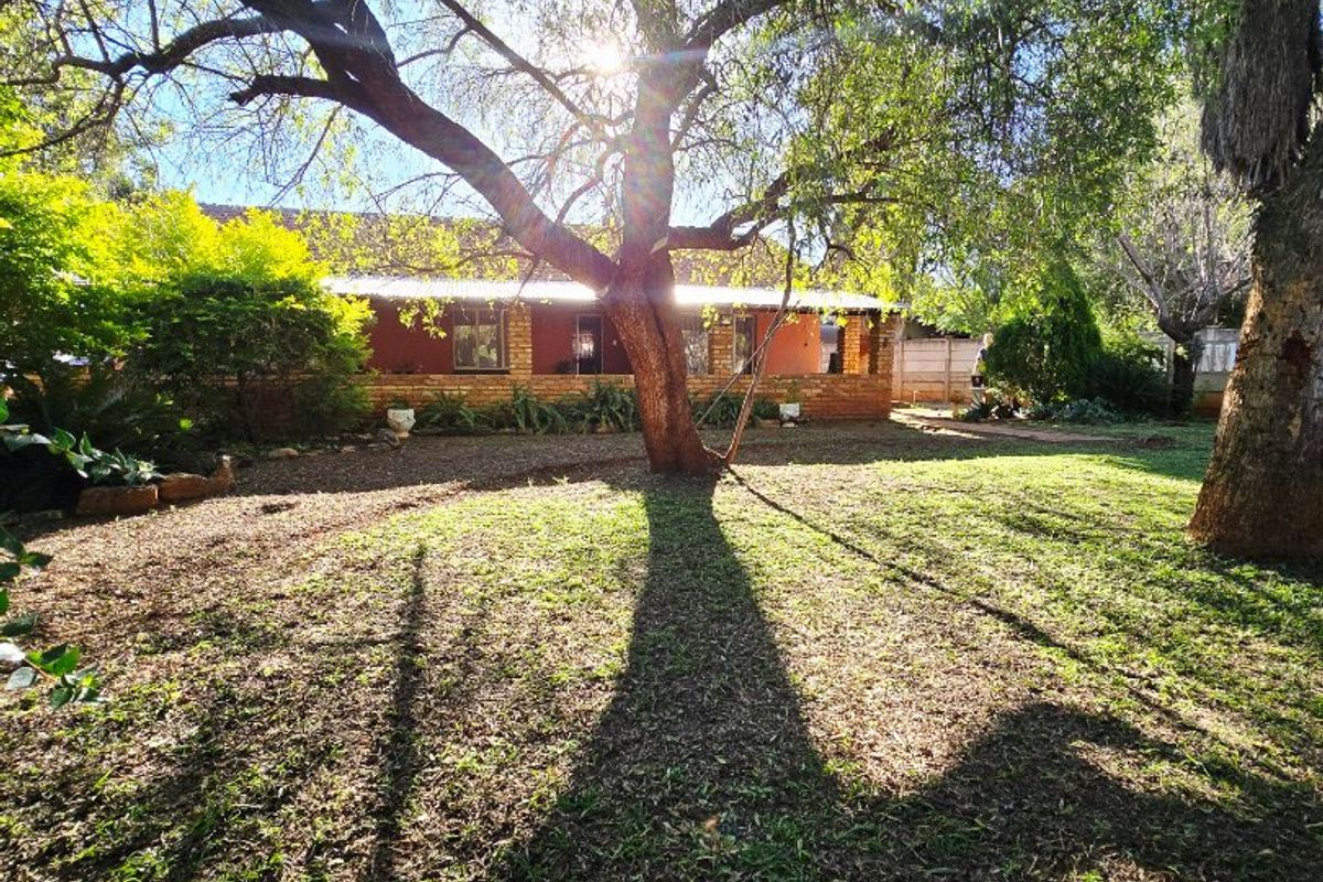 A spacious rear garden featuring mature trees and a view of the brick-built house with a covered patio area.