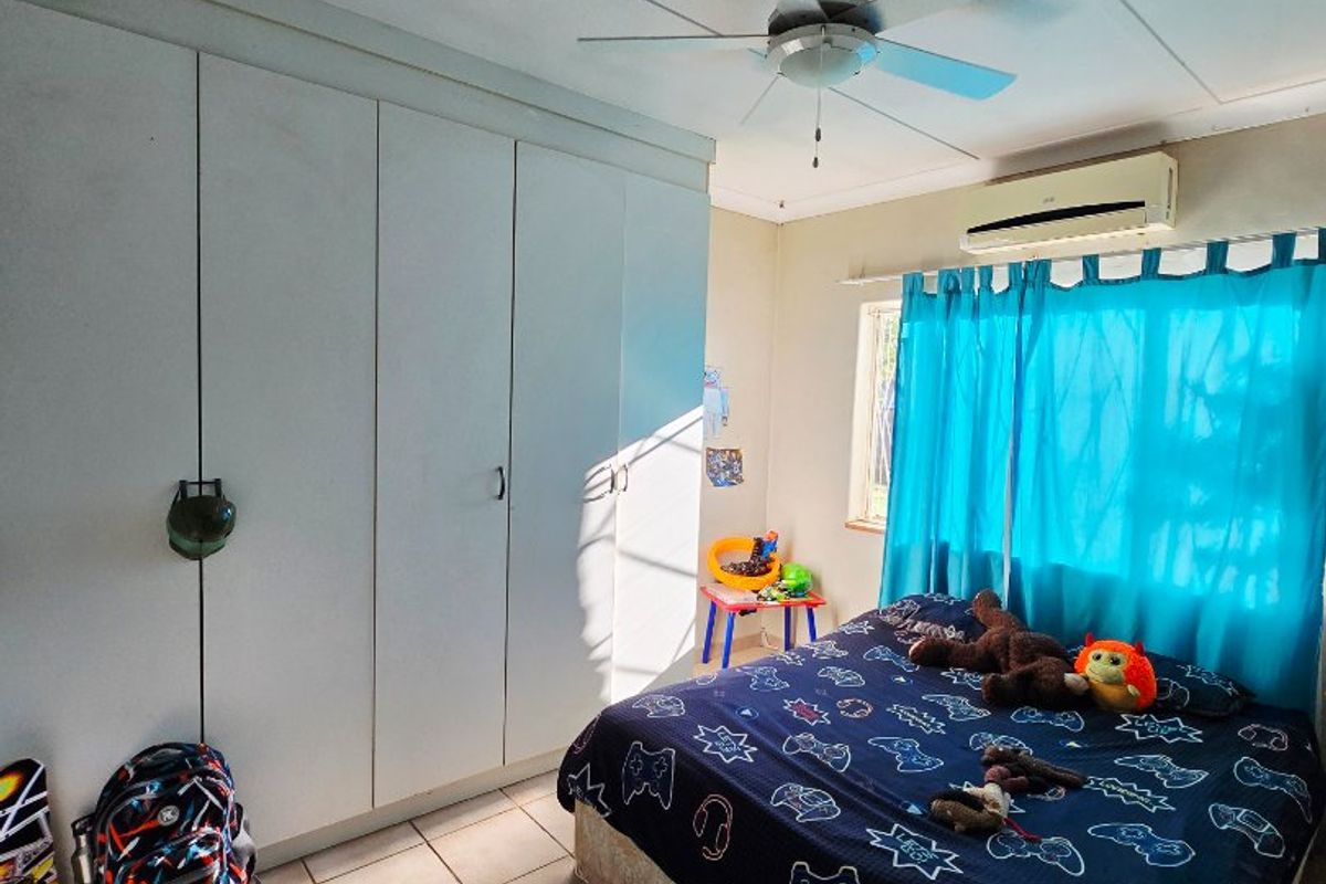 A bedroom featuring built-in cupboards, tiled flooring, a ceiling fan, and a wall-mounted split-system air conditioner.