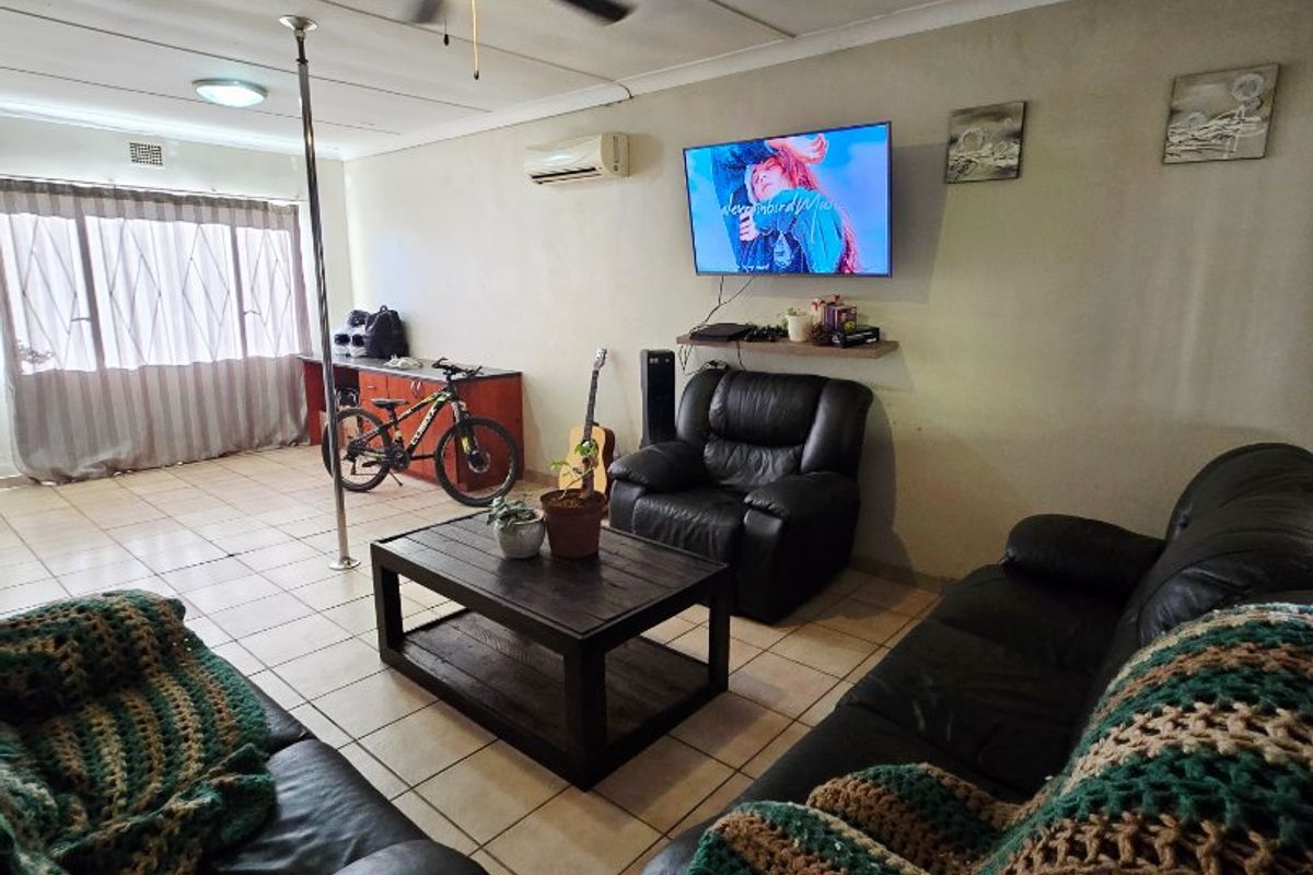 A spacious living room featuring tiled flooring, a ceiling fan, and a wall-mounted air conditioning unit, providing a functional and comfortable living space.