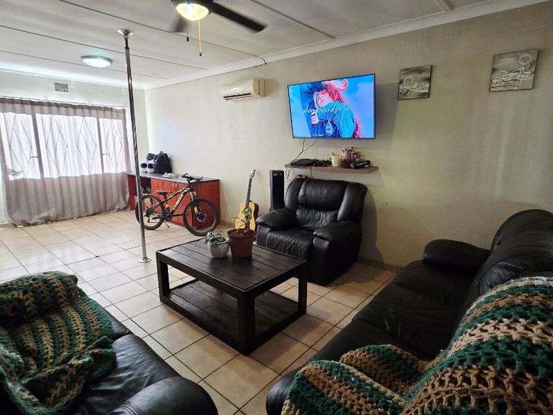 A spacious living room featuring tiled flooring, a ceiling fan, and a wall-mounted air conditioning unit, providing a functional and comfortable living space.