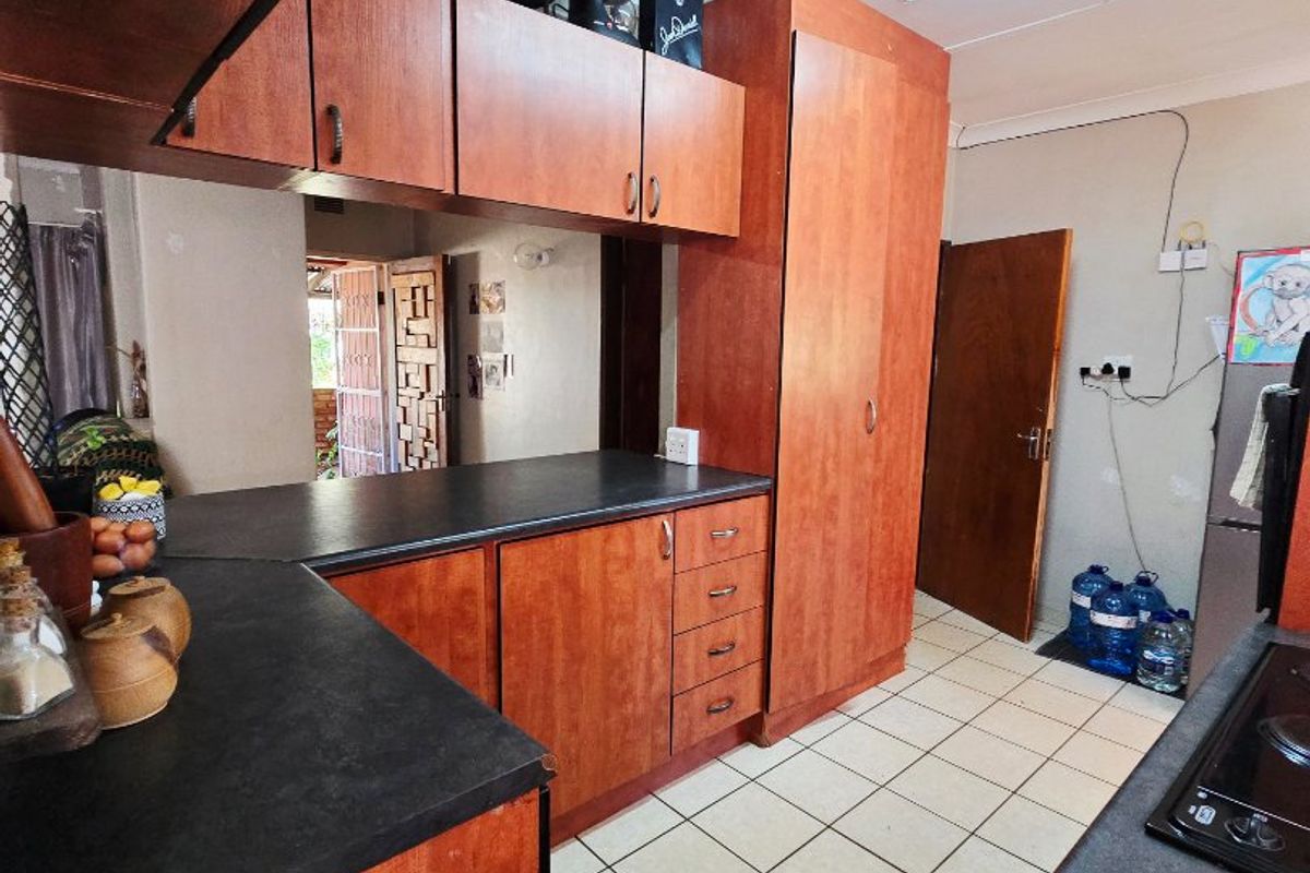 A functional kitchen featuring wood-look laminate cabinetry, dark countertops, and tiled flooring, requiring cosmetic updates to modernize the space.