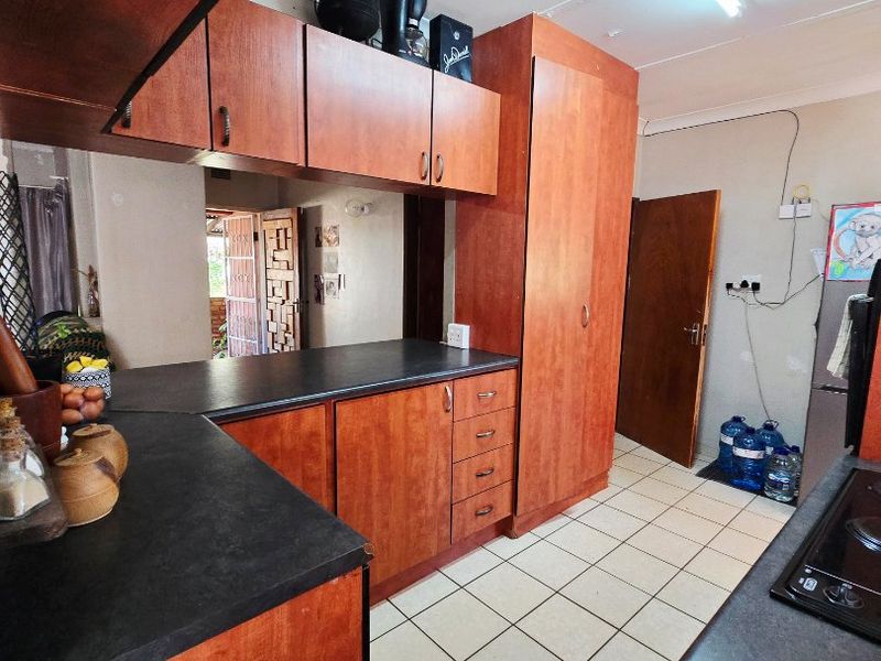 A functional kitchen featuring wood-look laminate cabinetry, dark countertops, and tiled flooring, requiring cosmetic updates to modernize the space.