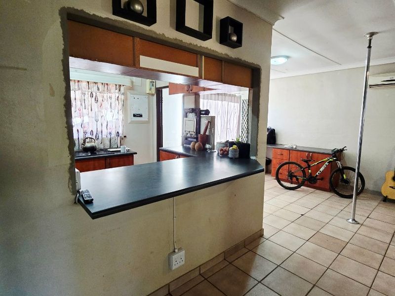 Open plan living area featuring a breakfast bar serving hatch connecting to the kitchen, tiled flooring, and an installed air conditioning unit.