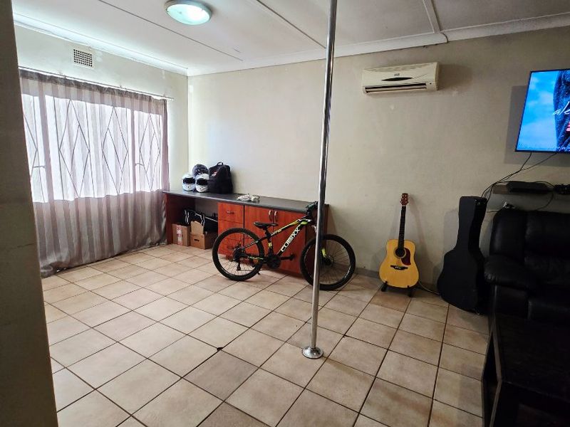 A living area featuring tiled flooring, a wall-mounted air conditioning unit, and built-in cabinetry, currently used as a multi-purpose space.