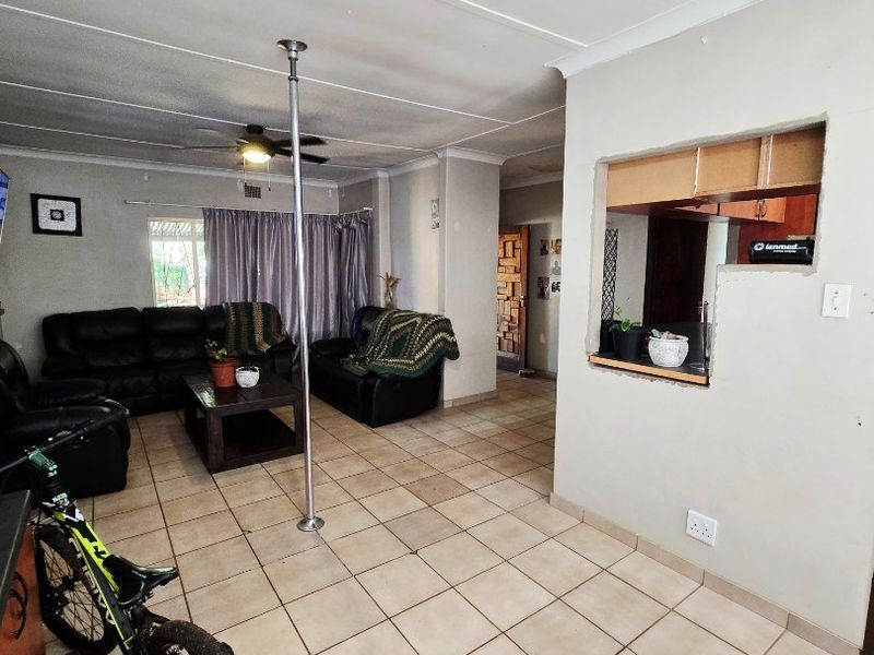 Open plan living area featuring tiled flooring, a ceiling fan, and a pass-through window opening into the kitchen area.