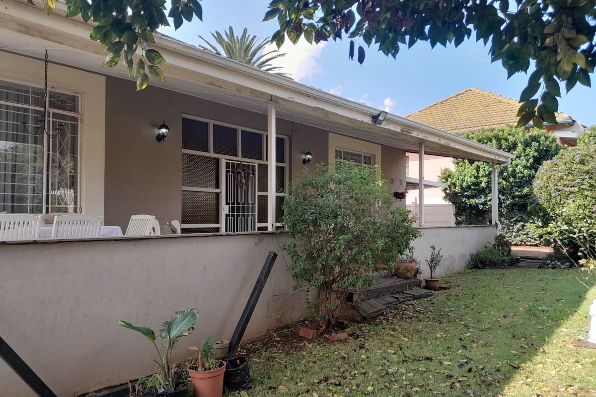 A rear exterior view of the house featuring a covered patio area with security gates and bars, showing signs of weathered exterior finishes.