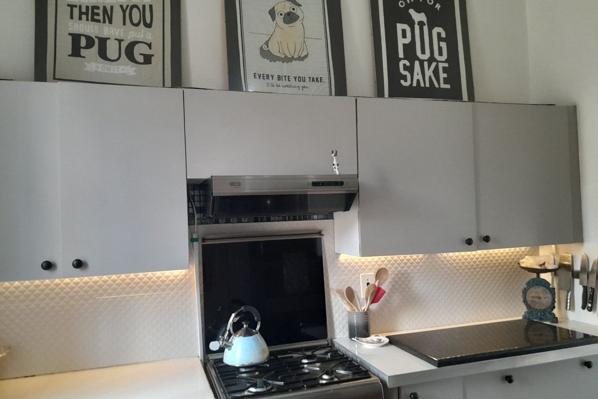 A functional kitchen featuring grey cabinetry, a gas hob with extractor fan, and a textured tile backsplash with integrated under-cabinet lighting.