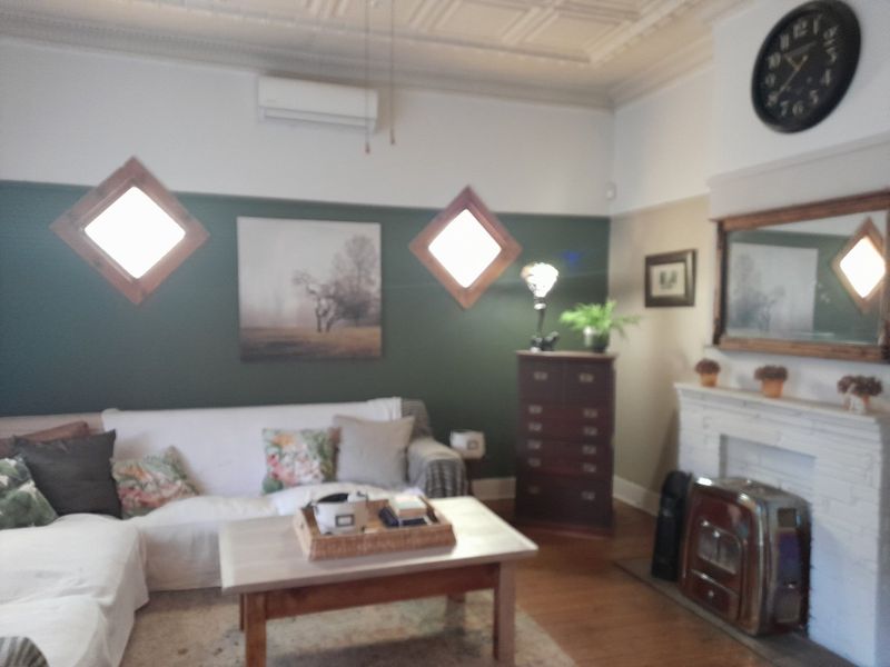 A cozy living room featuring a fireplace with a mantelpiece, unique diamond-shaped windows, timber flooring, and a decorative ceiling with an air conditioning unit.