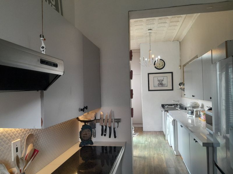A functional kitchen featuring built-in cabinetry, a hob with extractor fan, and a tiled splashback, leading into a secondary utility or scullery area.