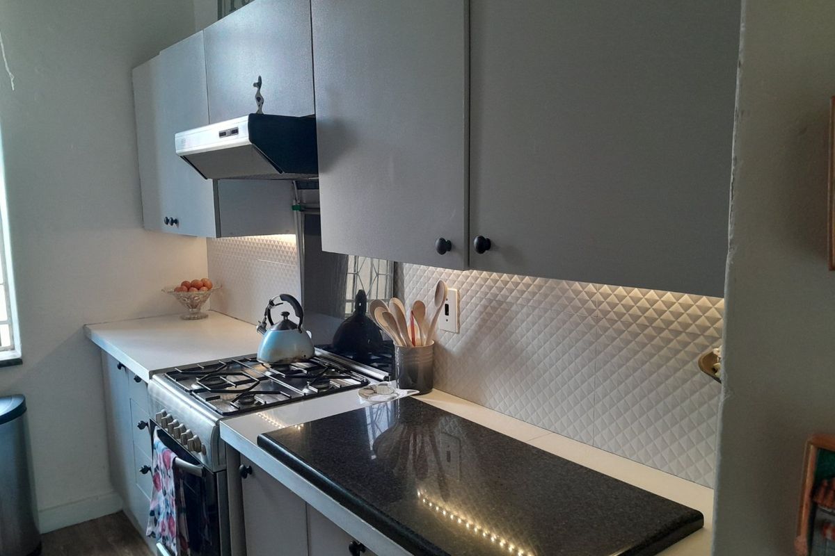 A functional kitchen featuring grey cabinetry, a gas cooktop with extractor fan, textured tile backsplash, and a mix of laminate and granite countertops.