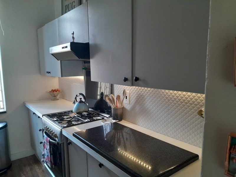 A functional kitchen featuring grey cabinetry, a gas cooktop with extractor fan, textured tile backsplash, and a mix of laminate and granite countertops.