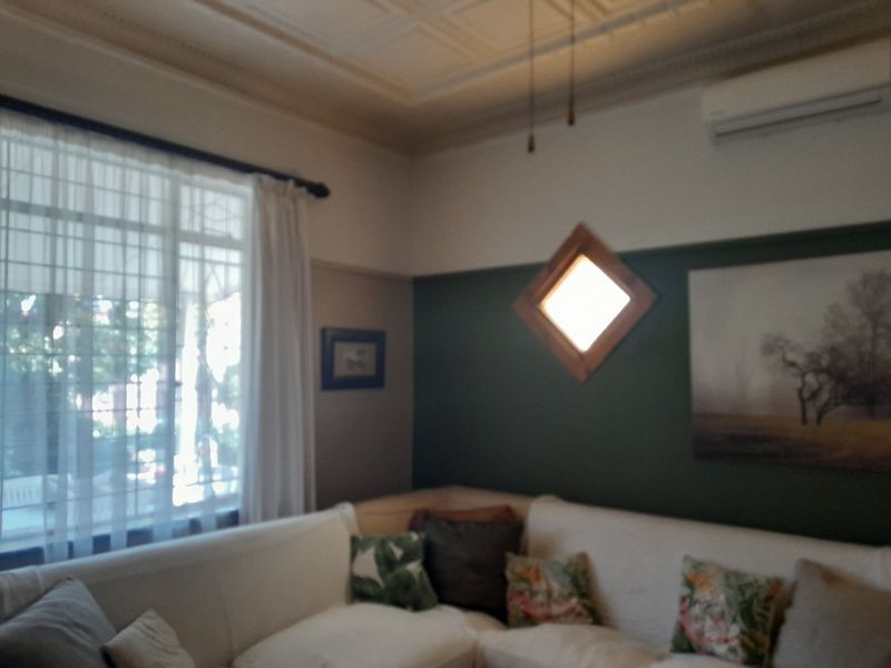 A living room featuring a classic pressed metal ceiling, a split system air conditioner, and a unique diamond-shaped feature window.