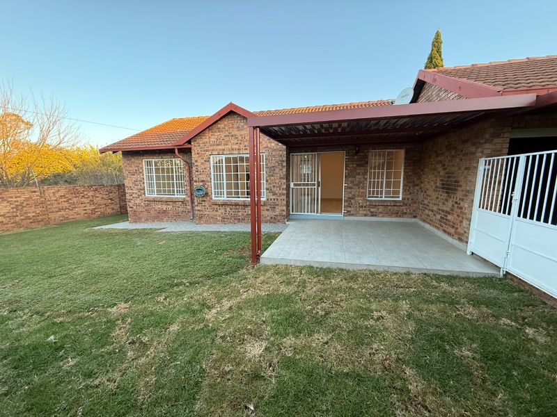 Rear view of the townhouse featuring a brick facade, tiled roof, covered patio area, and a private garden with a brick boundary wall.