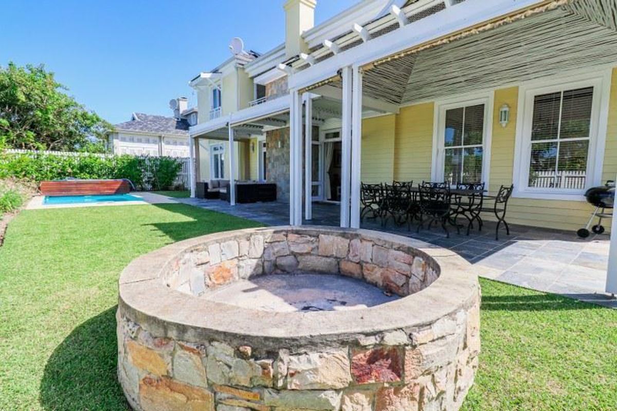 Spacious rear garden featuring a stone fire pit, covered patio with pergola, and a swimming pool, ideal for outdoor entertaining.