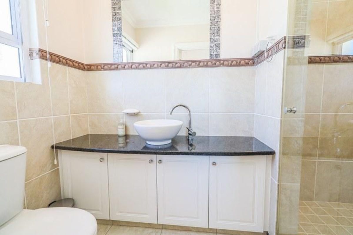 A well-maintained bathroom featuring a modern vessel sink on a granite vanity, white cabinetry, and a glass-enclosed shower with neutral ceramic tiling.