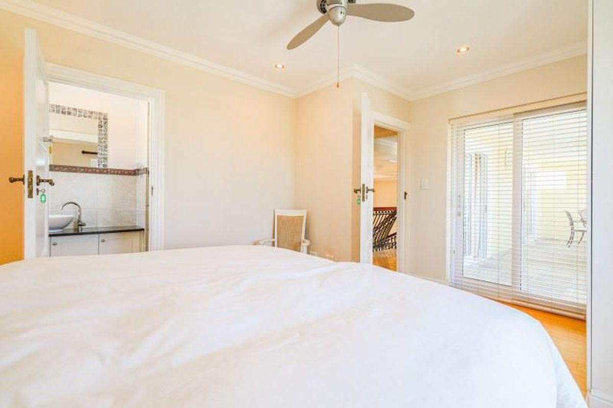 A bright bedroom featuring a ceiling fan, crown molding, and sliding glass doors leading to an outdoor area, with an adjoining en-suite bathroom.