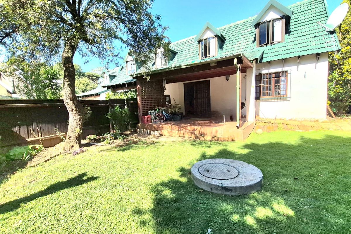 Rear view of the townhouse featuring a covered patio, green tiled roof with dormer windows, and a private garden area.