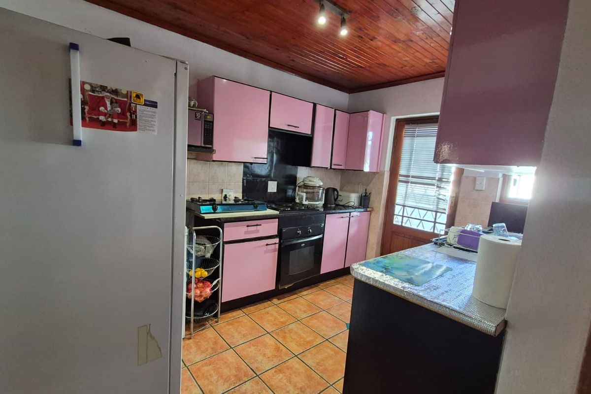 A dated kitchen featuring pink cabinetry, gas hob, built-in oven, and timber ceiling, offering potential for a modern renovation.