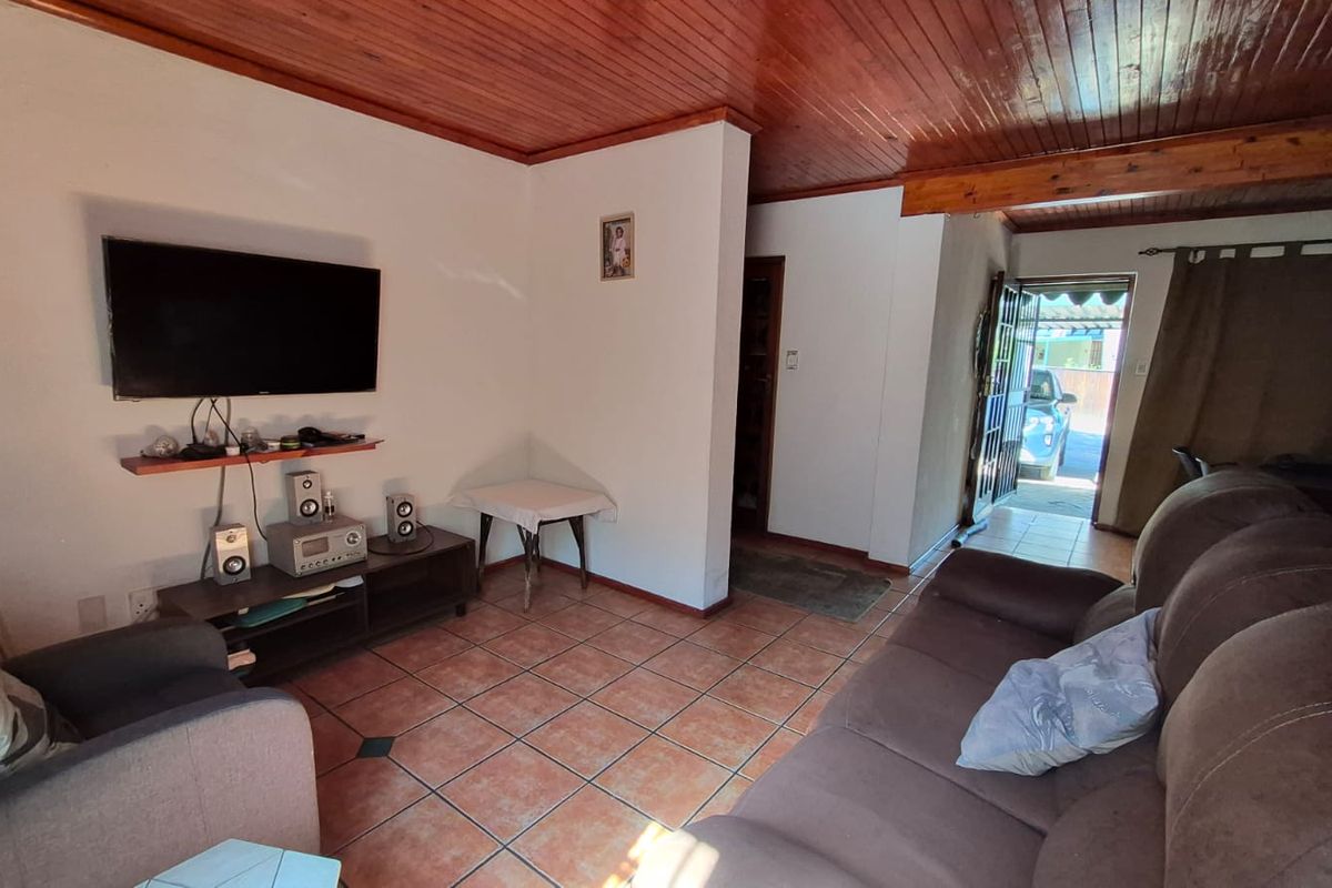 A living room featuring a timber tongue and groove ceiling and ceramic tiled flooring, with direct access to the exterior through a security gate.