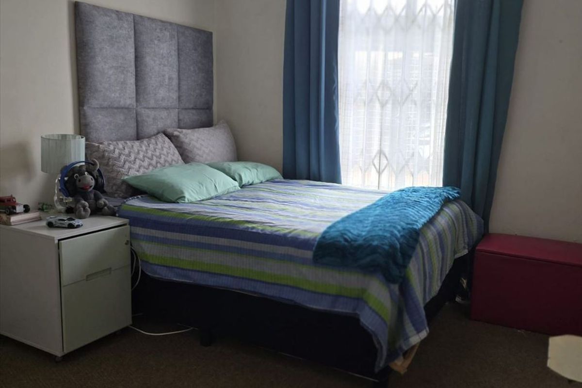 A standard bedroom featuring a window with curtain rod and ventilation grille, providing a functional space for rest.