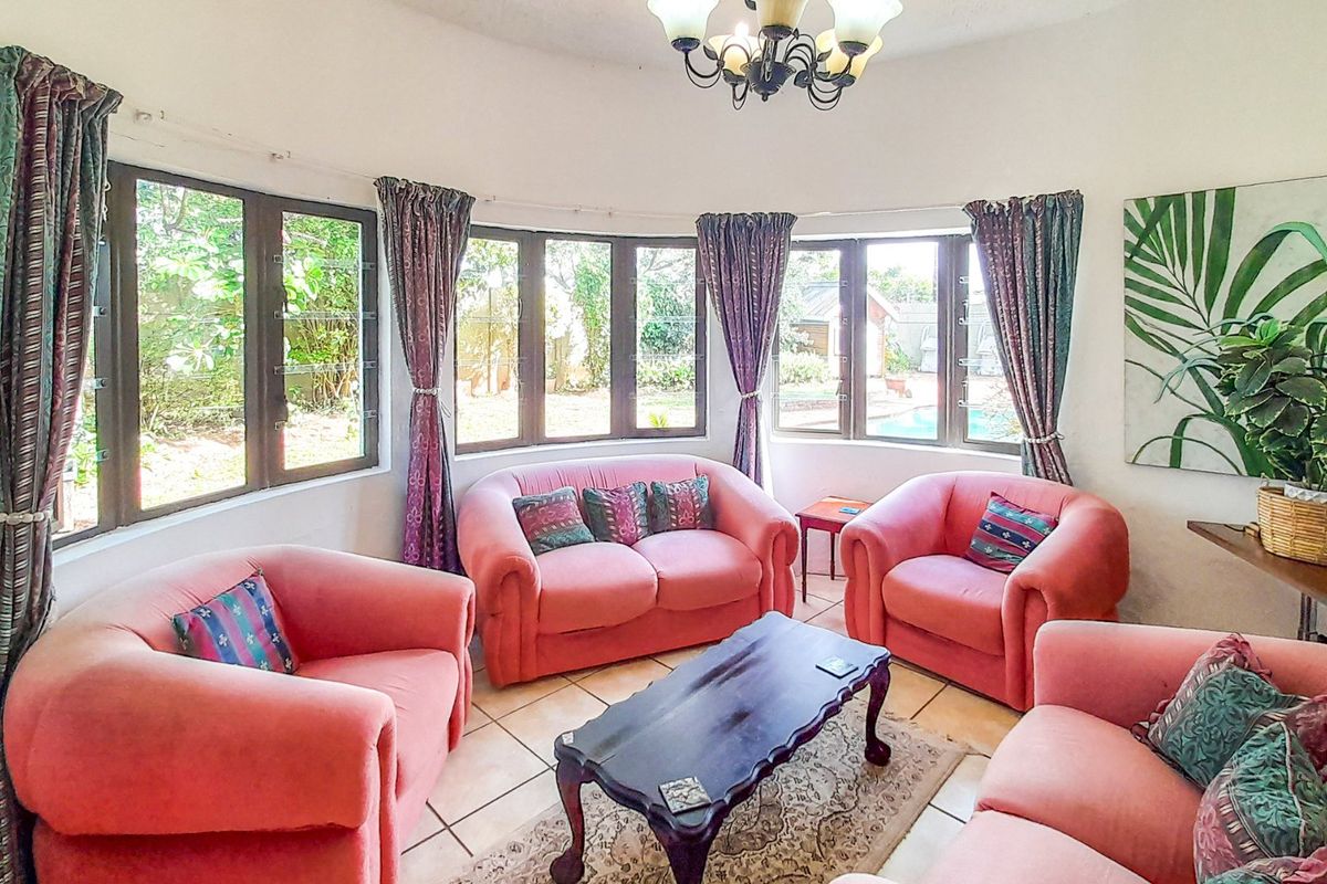 A bright living room featuring a curved bay window with garden views, tiled flooring, and a classic wrought iron chandelier.